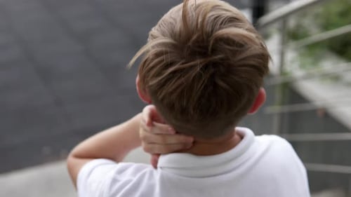 Boy Rubbing Neck Outside in Mid Shot