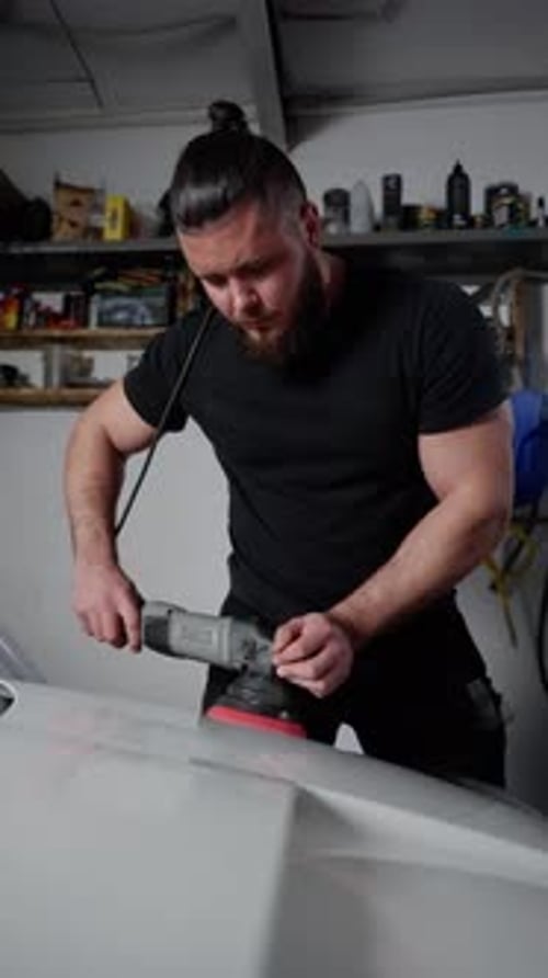 A Man is Polishing a Car with a Buffing Machine He is Wearing a Black Shirt and Has a Beard