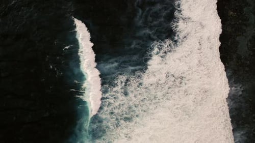 Aerial birds eye view of dramatic dark moody ocean water with white waves breaking
