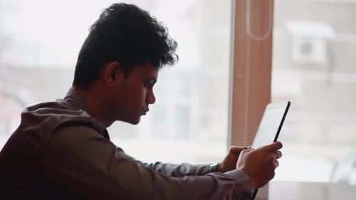 Young Man Using Tablet Device Indoors by Window
