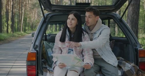 Young Couple Looking at Map in Car Trunk
