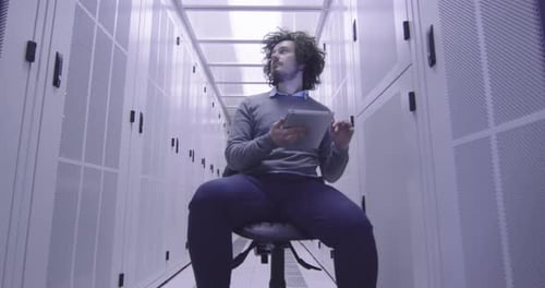 Adult Sitting in Server Room Using Tablet