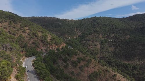 An aerial view of a winding mountain road cutting through a rugged landscape covered with dense