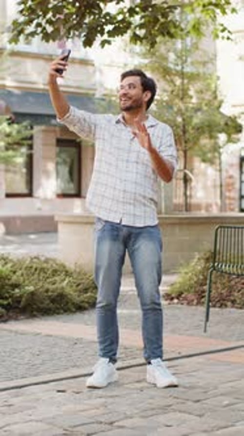 Cheerful Indian Man Blogger Taking Selfie on Smartphone Talking Video Call Standing on City Street