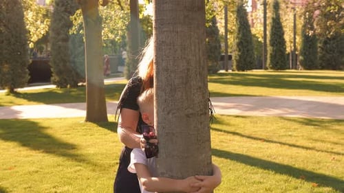 Closeup of a Mother with Her Son Peeking Out From Behind a Tree in a Park