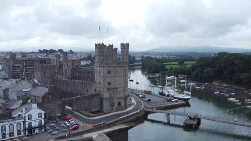 Ancient Caernarfon castle Welsh harbour town aerial view medieval waterfront landmark wide orbit rig