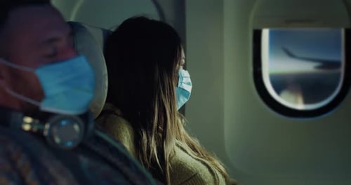 Cinematic shot of young couple wearing medical masks in aircraft while traveling with com