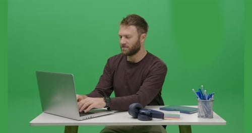 Uoung Caucasian man is using his laptop in a frontal view, captured in a portrait shot with a green