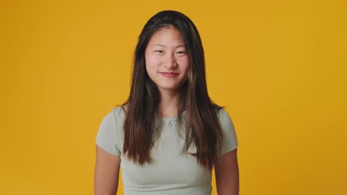 Young woman looking at camera showing thumbs up isolated on yellow background in studio