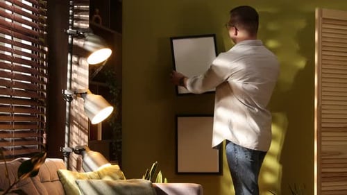 Decorator hanging picture frame on olive wall indoors
