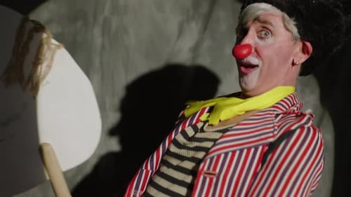 Silly Clown in Black Hat Riding Stick Horse during Circus Performance