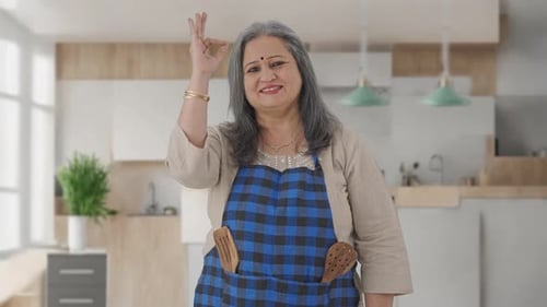 Woman in Kitchen Smiles and Makes Okay Sign
