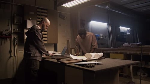 Furniture Makers Working with Laptop and Blueprint in Carpentry Workshop