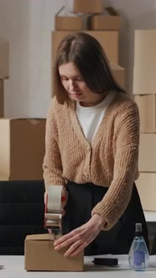 Young Woman Taping Boxes at Desk for Shipping