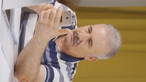 Vertical video of Home office worker old man having problems and stress on the phone.