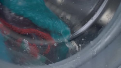 Close up slow motion washing machine spinning blue cotton towels soaking bubbles glass door detergen