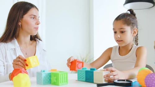 Speech Therapist Engages with Child Using Colorful Building Blocks to Enhance Communication Skills