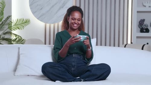 Happy Woman Plays Mobile Game on Sofa