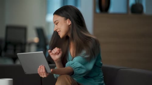Festive asian businesswoman dancing with tablet celebrates success at luxury office
