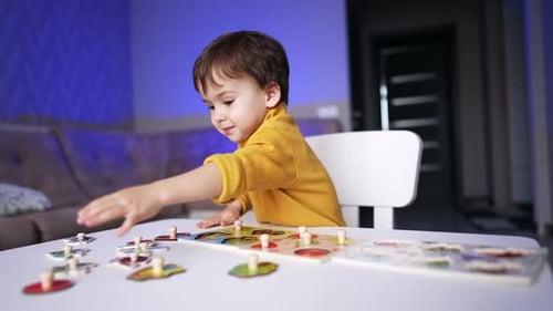 Baby boy in yellow sweater reaches for a puzzle piece. Toddler kid playing with puzzles at home.