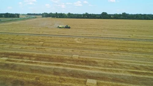 Hay Baler Tractor Driving Across the Field Collecting Straws and Making the Bales Aerial Scenery in