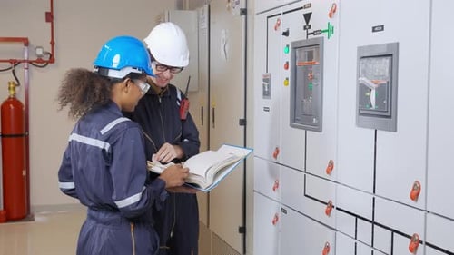 Technicians Reviewing Paperwork Next to Control Panel