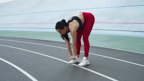 Attractive young woman stretching body at modern stadium athletics track