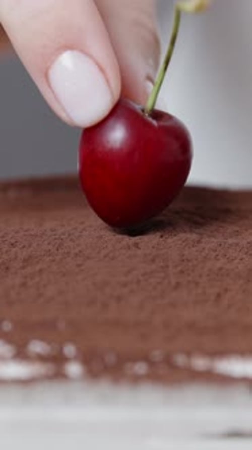 A cherry is placed on top of the tiramisu with cocoa powder. Close-up. Vertical video.