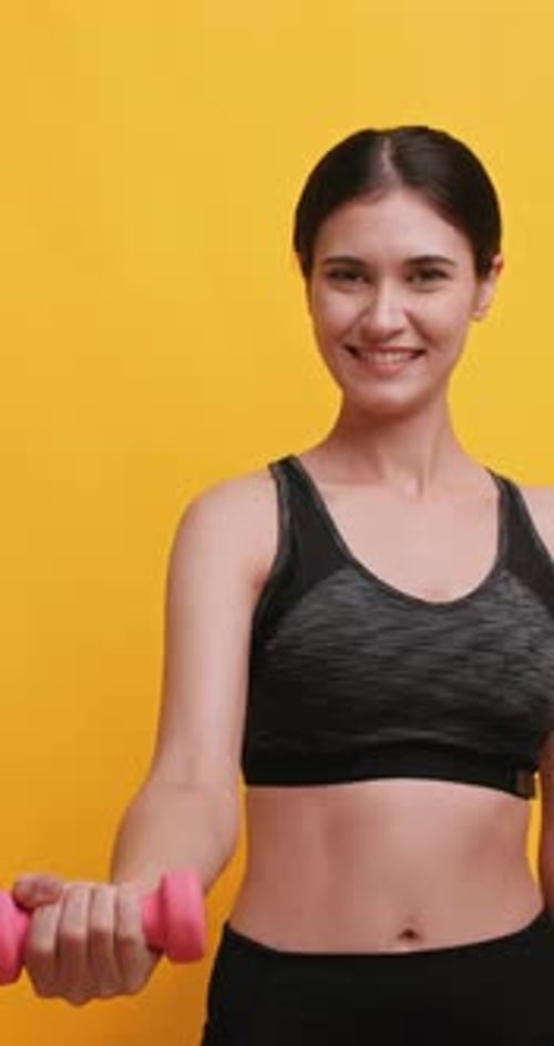 Vertical clip. Young sportswoman shows off her physical strength by lifting dumbbell.