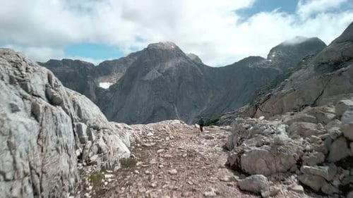 Hiker coming to the camera while the drone passes through letting you see a remote valley.