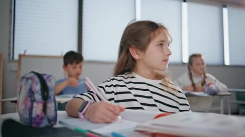 Elementary Student Writing at Desk in Classroom