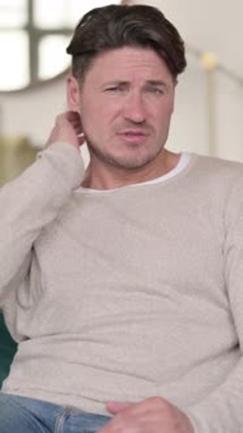 Man Massaging Sore Neck While Sitting Indoors