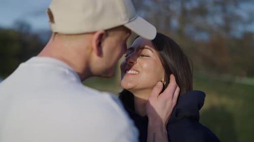 Lovely couple at park, guy gently touch cheek and kiss girlfriend on lips