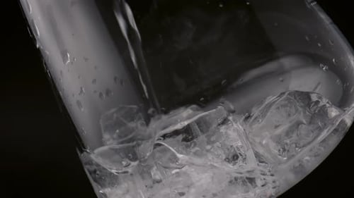 Thin water trickle fills glass with ice cubes creating a refreshing drink