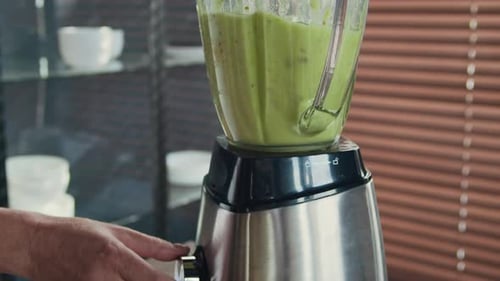 Anonyme Hausfrau bereitet grünen Smoothie im Mixer in der heimischen Küche zu