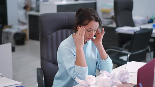 A Focused Woman in an Office Surrounded By Crumpled Paper and Busy with Her Tasks