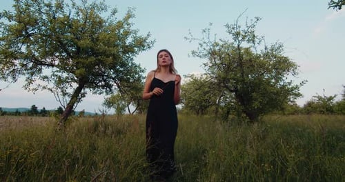 Female blonde model in black long dress walking in an apple garden or orchard