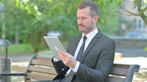 Man Using Tablet on Bench in City Park
