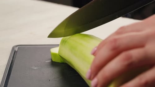 Young Green Zucchini are Cut with a Knife on a Wooden Board on the Table