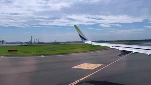 Airplane taxiing on the runway with wing visible under bright skies near airport terminal