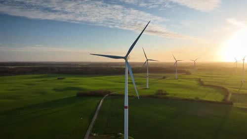 Aerial footage of large spinning wind turbine in agriculture fields with sunrise.