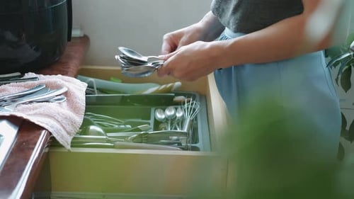 Woman Arranges Silverware in Kitchen Drawer at Home