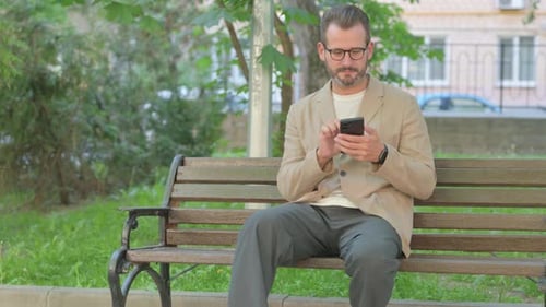 Man Using Smartphone on Park Bench