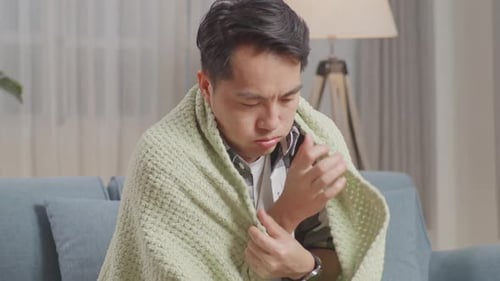 Gros plan d'un homme asiatique malade avec une couverture gelée et frissonnant sur le canapé dans le salon à la maison