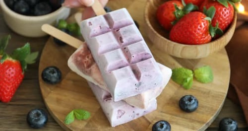 Woman taking delicious yogurt popsicles, blueberries, strawberries and mint at wooden table, closeup