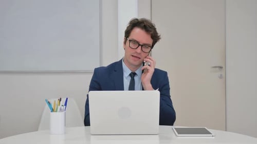 Man in Suit Using Laptop and Talking on Phone