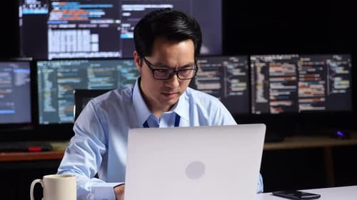 Programmeur asiatique écrivant du code par un ordinateur portable à l'aide de plusieurs moniteurs affichant une base de données