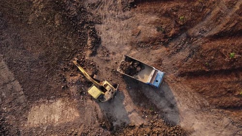 Aerial view of a wheel loader excavator with a backhoe loading sand into a heavy earthmover