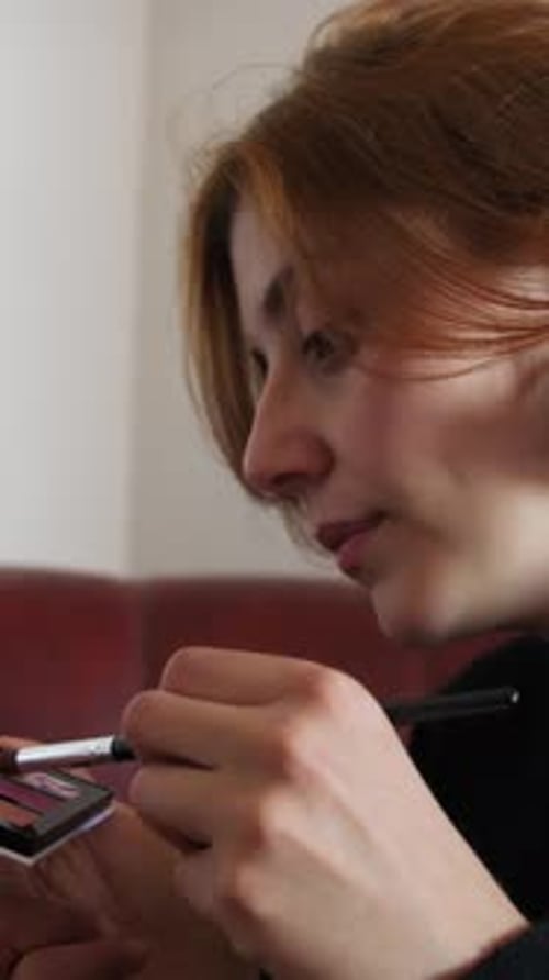 Young Adult Applies Makeup with Brush Indoors