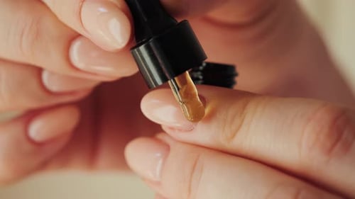 Woman applying nourishing moisturizing oil on cuticles after manicure.